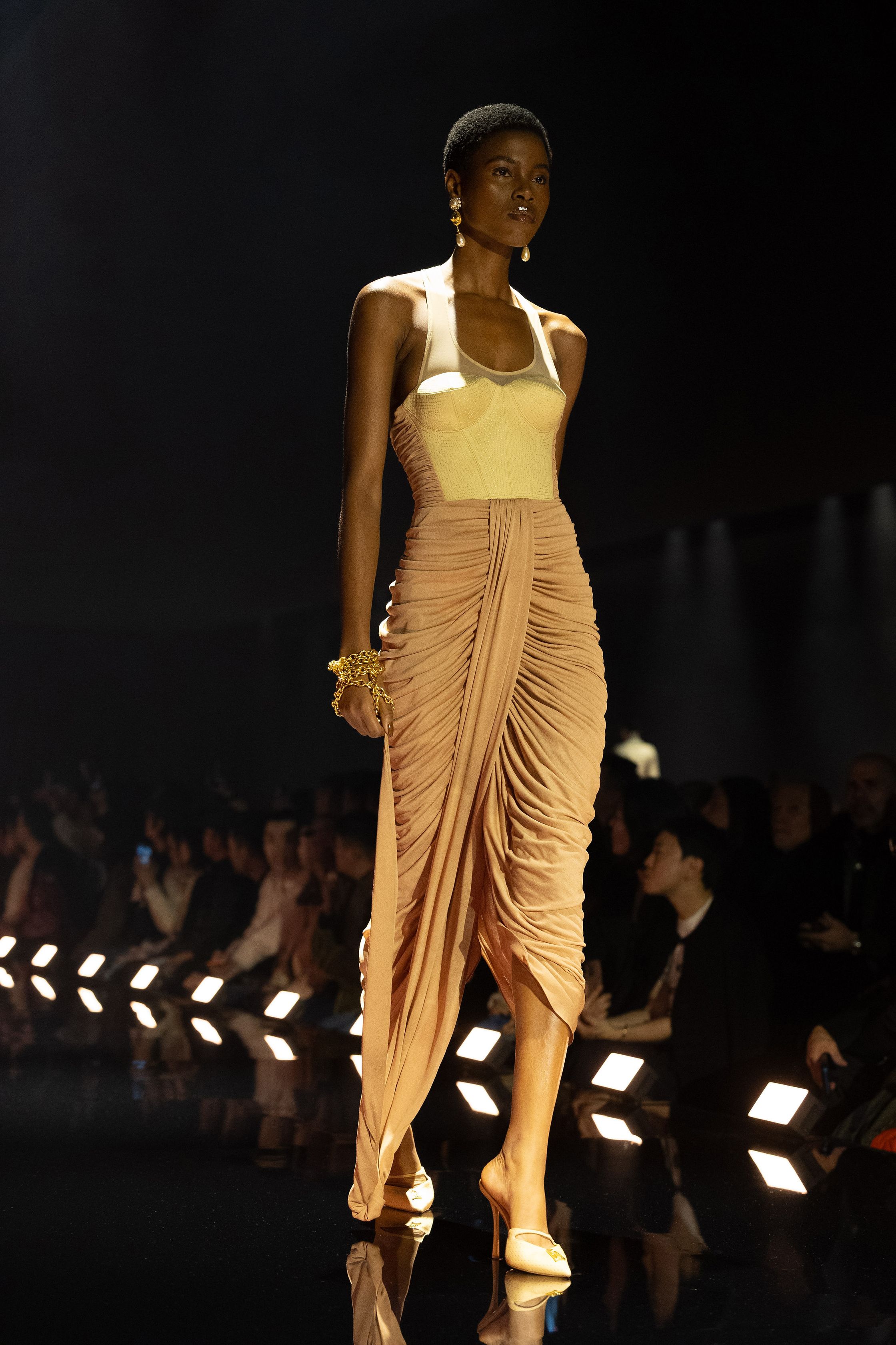 Schiaparelli 2026秋冬系列延续品牌标志性的超现实主义美学，在金色灯光的T台上呈现极具雕塑感的廓形。沙金色与黑金色成为主调，褶皱礼服、雕塑式西装与高腰裙装强化身体线条。经典的金属装饰、夸张肩线以及精致刺绣细节构成强烈视觉符号，使整场秀既华丽又充满戏剧张力。设计师通过结构与面料的张力对比，让高级定制的艺术精神融入现代女性衣橱-顽石频道趋势研究